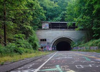 38 Abandoned Places in PA You Can Legally Explore Entrance to the abandoned Rays Hill Tunnel along the Pennsylvania Turnpike in Bedford County, Pennsylvania, with colorful graffiti and chalk drawings covering the roadway leading into the dark tunnel beneath a wooded hillside.