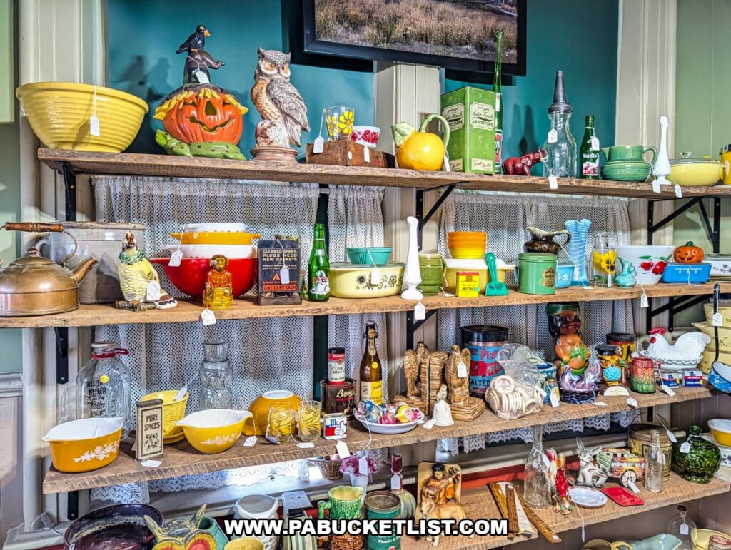 Wooden wall shelves inside Sunbury Station Antiques in Northumberland County, Pennsylvania, displaying colorful vintage kitchenware, Pyrex bowls, glass bottles, tins, figurines, and retro home decor arranged within the historic train station building.