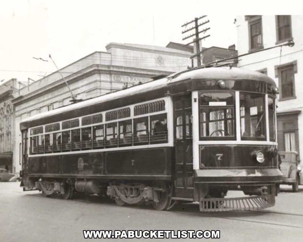 Black-and-white photograph of a vintage electric streetcar stopped on a Pennsylvania city street, showing its enclosed passenger cabin, overhead trolley pole, steel wheels on tracks, and surrounding early 20th-century buildings.