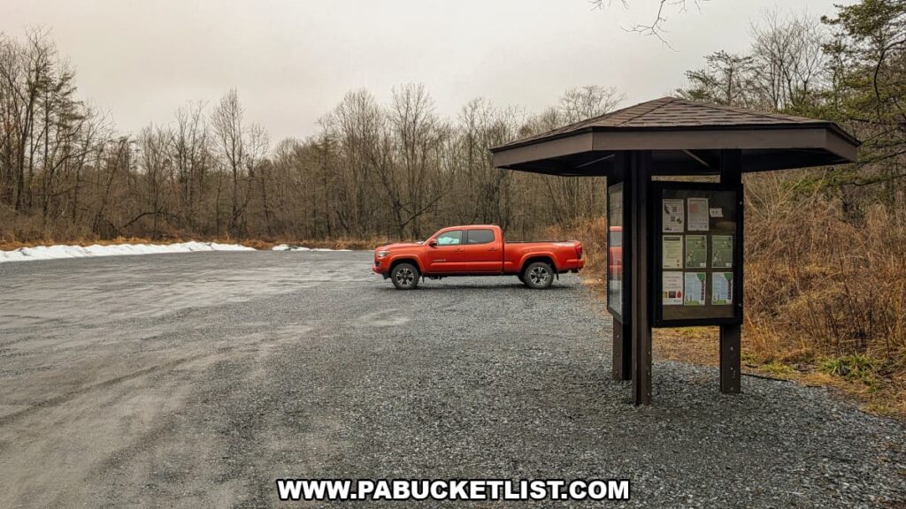 Gravel parking area and trailhead information kiosk near Bordner Cabin in Swatara State Park, Lebanon County, Pennsylvania, with forested surroundings in late winter.