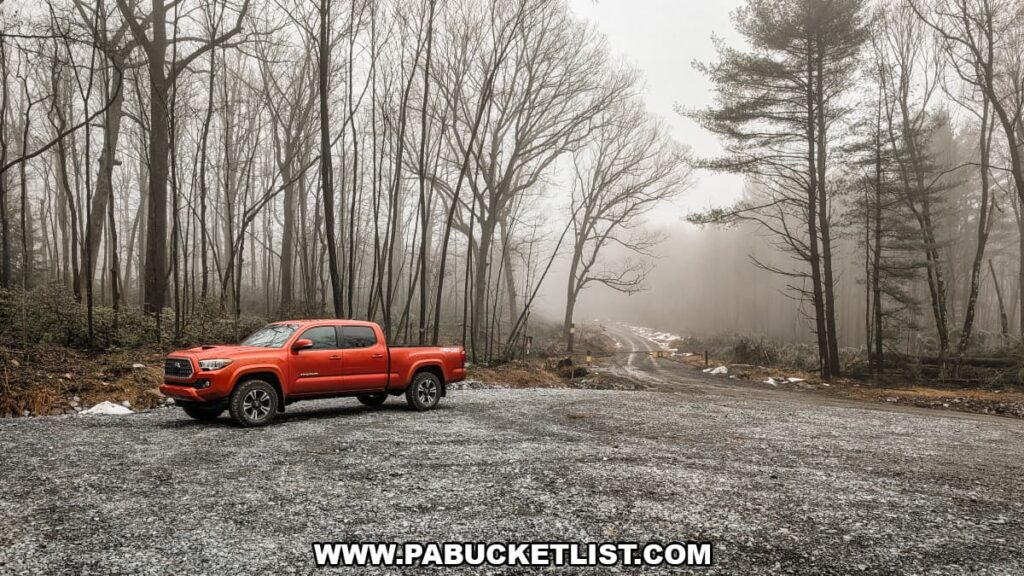 Gravel parking area near the Boxcar Rocks trailhead on State Game Lands 211 in Lebanon County, Pennsylvania, with a forest road disappearing into fog among tall trees.