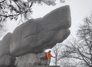 Hiker standing beneath a massive stacked conglomerate boulder at Boxcar Rocks on State Game Lands 211 in Lebanon County, Pennsylvania, with fog drifting through the surrounding forest.