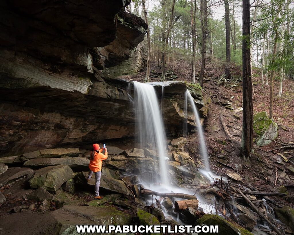Photographer standing beneath the rock overhang photographing Kildoo Falls at McConnells Mill State Park in Lawrence County, Pennsylvania.