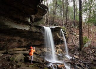 Photographer standing beneath the rock overhang photographing Kildoo Falls at McConnells Mill State Park in Lawrence County, Pennsylvania.