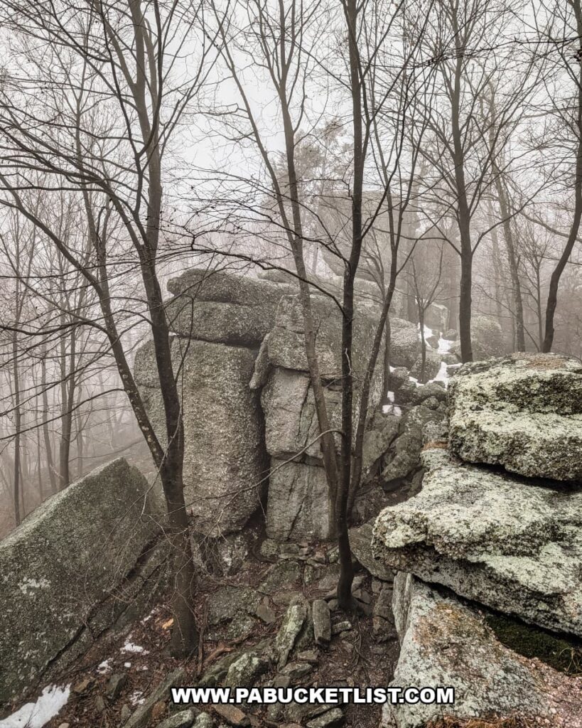 Stacked conglomerate boulders forming part of the Boxcar Rocks outcropping on Sharp Ridge in Lebanon County, Pennsylvania, surrounded by leafless trees in a foggy forest.
