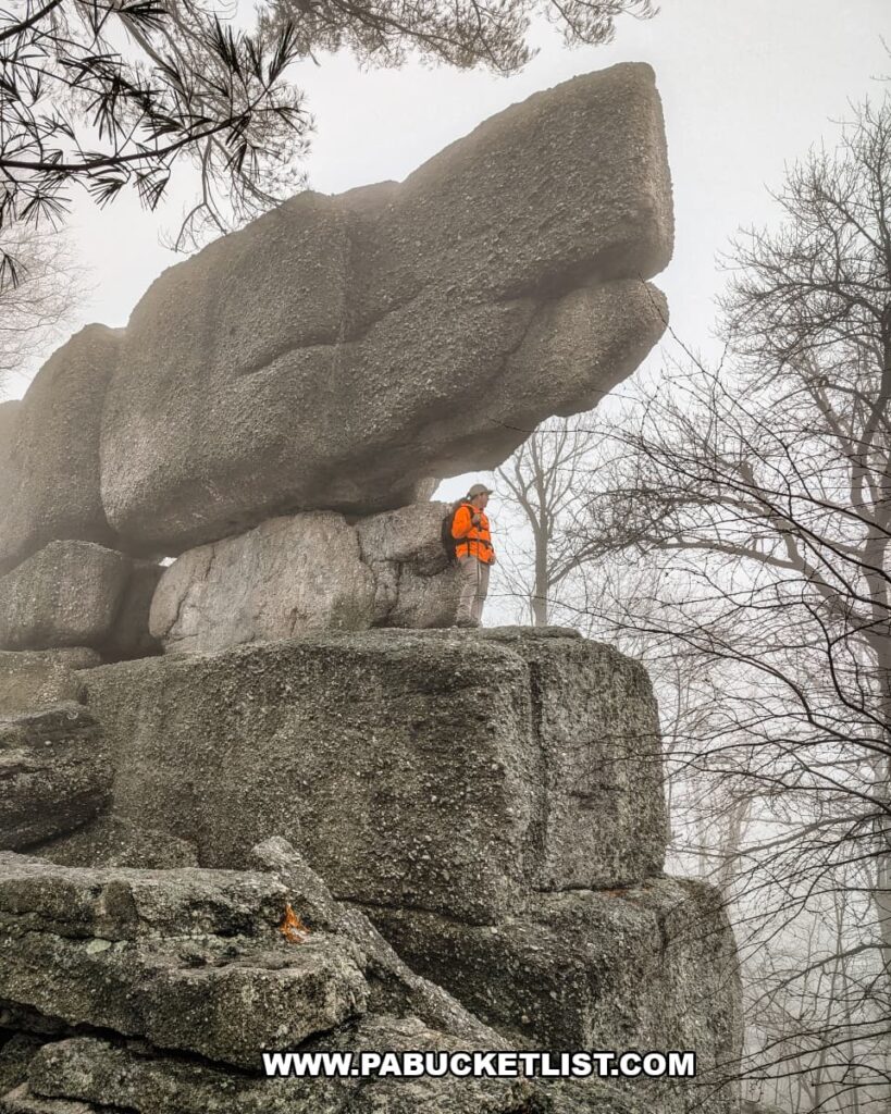 Hiker standing beneath massive stacked conglomerate boulders at Boxcar Rocks in Lebanon County, Pennsylvania, with fog drifting through the surrounding forest.