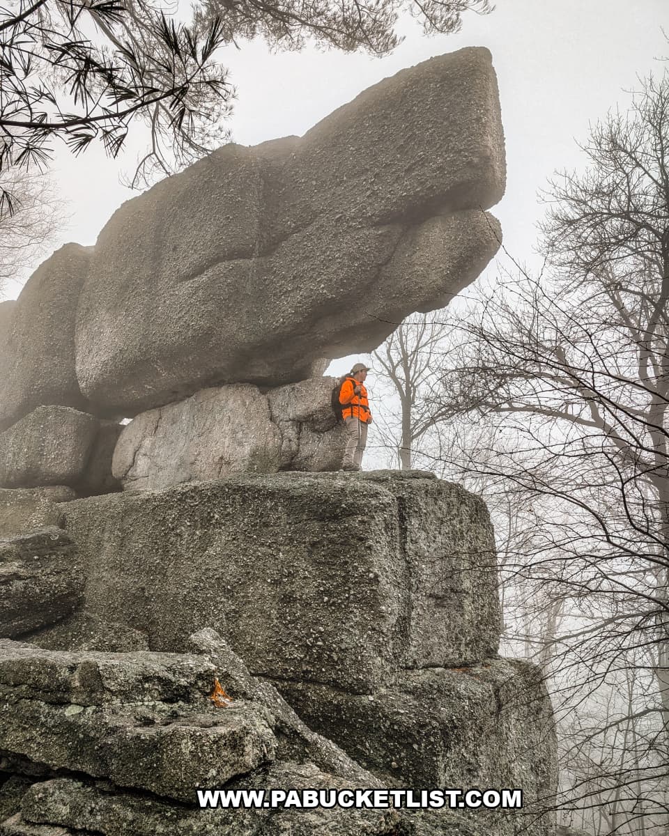 Hiker standing beneath massive stacked conglomerate boulders at Boxcar Rocks in Lebanon County, Pennsylvania, with fog drifting through the surrounding forest.