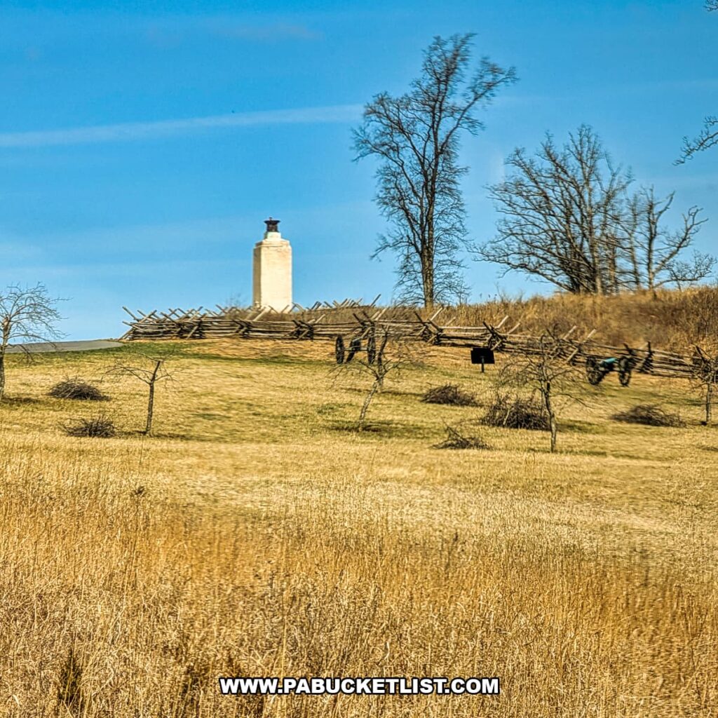 Civil War cannons and split-rail fencing below a stone battlefield monument at Gettysburg National Military Park, viewed from a Gettysburg Railway sightseeing train excursion in Gettysburg, Pennsylvania.