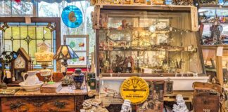 Vintage curio cabinet filled with collectibles alongside antique furniture, lamps, and stained glass inside Wagon Wheel Antiques in Butler County, Pennsylvania.