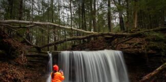 Photographer standing beside Grindstone Falls capturing images of the waterfall along an unnamed tributary of Grindstone Run at McConnells Mill State Park in Lawrence County, Pennsylvania.