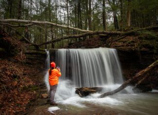 Photographer standing beside Grindstone Falls capturing images of the waterfall along an unnamed tributary of Grindstone Run at McConnells Mill State Park in Lawrence County, Pennsylvania.