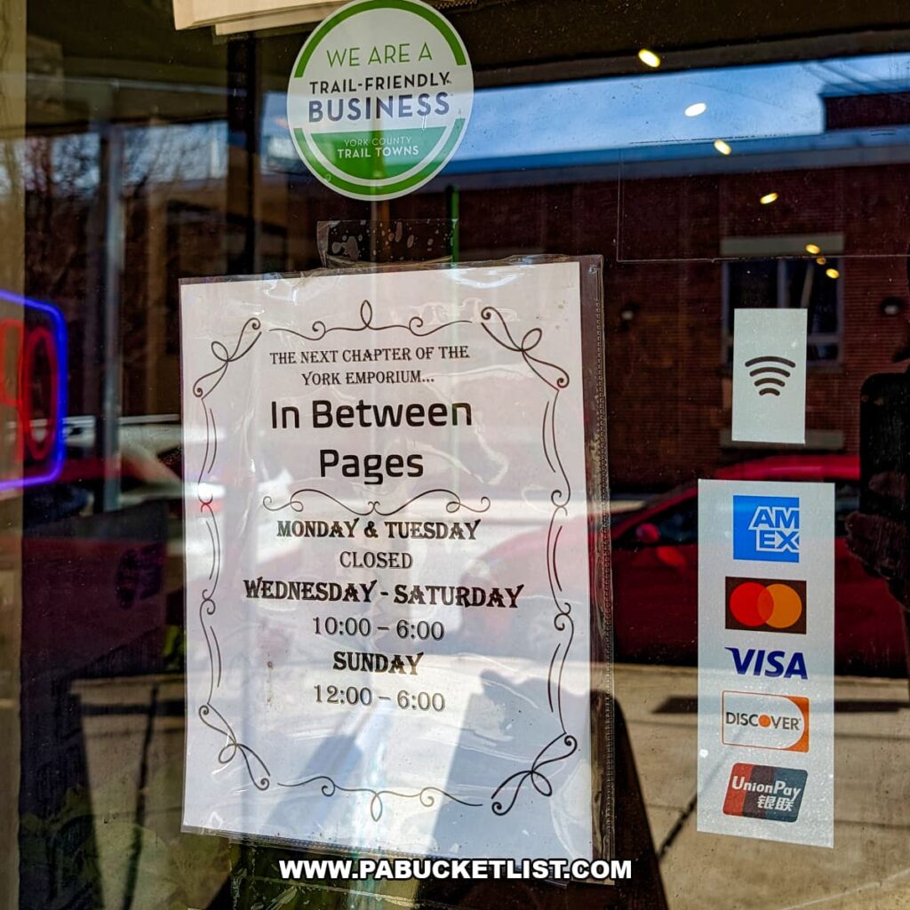 Store hours sign on the door at In Between Pages Bookstore in York PA noting the next chapter of the York Emporium and listing weekly hours