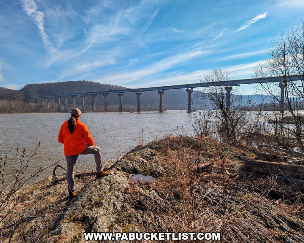 Visitor standing on rocky shoreline at the Lock 12 Historic Area overlooking the Susquehanna River and the Norman Wood Bridge in York County, Pennsylvania.