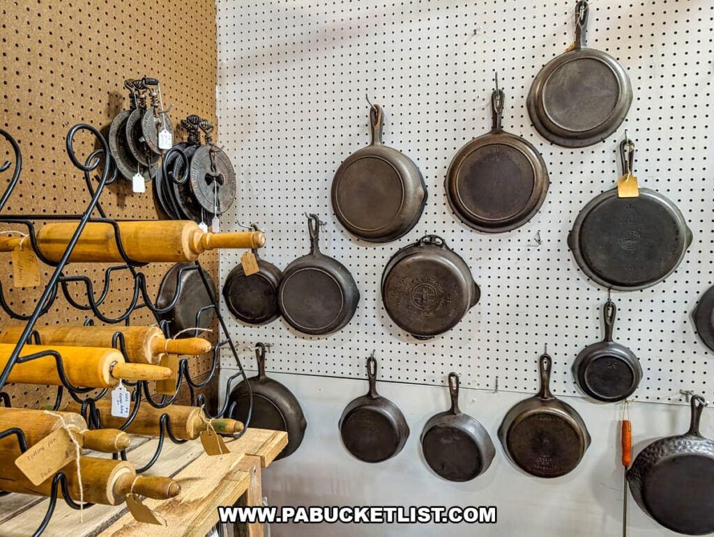 Display of vintage cast iron skillets hanging on a pegboard with antique rolling pins at Pen-Mar Antique Market in Waynesboro Pennsylvania