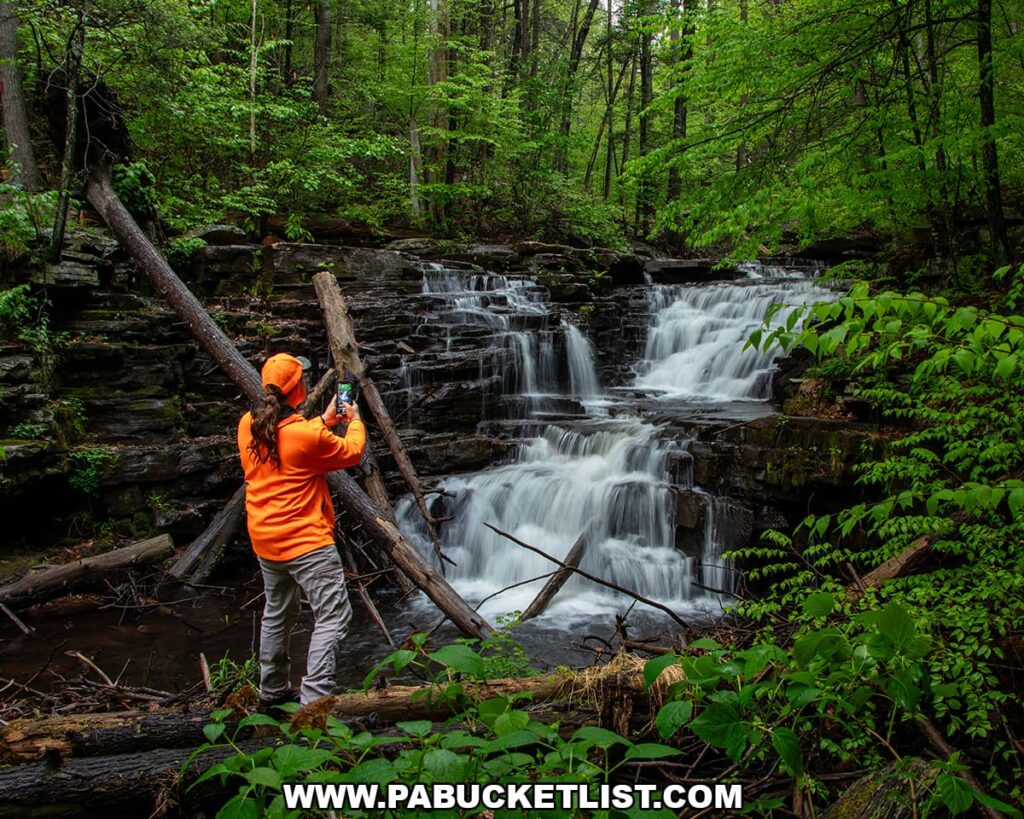 Photographer standing beside Jarrett Falls capturing images of the waterfall cascading over layered rock ledges in Fulton County, Pennsylvania