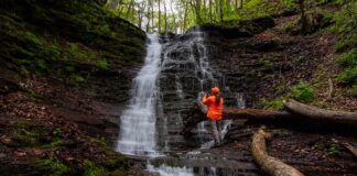 Photographer standing beside Rail Island Run Falls as the 20-foot-tall waterfall cascades over layered rock ledges in Tioga County, Pennsylvania.