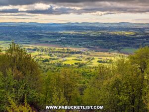 sunlit patchwork farmland and rolling hills viewed from waggoners gap hawk watch in perry county pennsylvania framed by spring forest under dramatic clouds