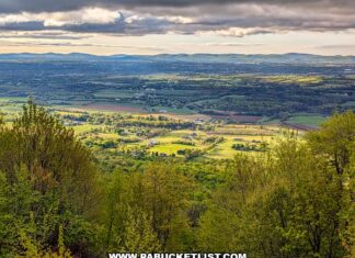 sunlit patchwork farmland and rolling hills viewed from waggoners gap hawk watch in perry county pennsylvania framed by spring forest under dramatic clouds
