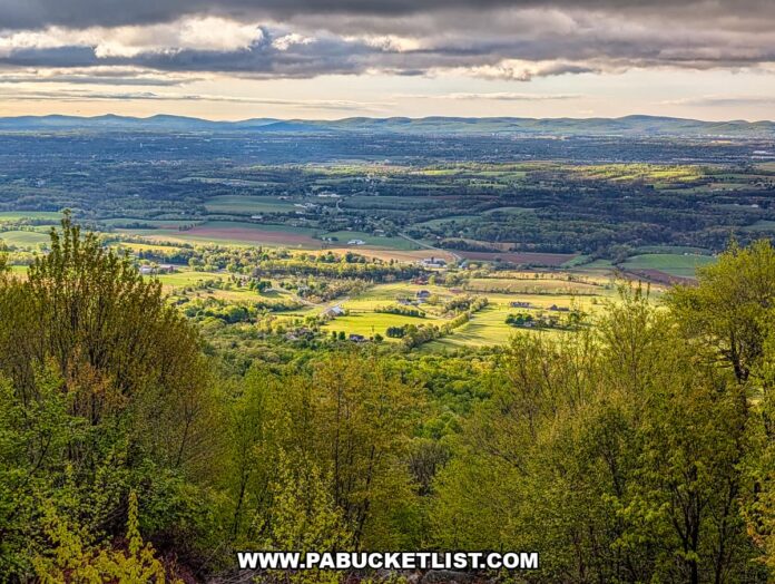 sunlit patchwork farmland and rolling hills viewed from waggoners gap hawk watch in perry county pennsylvania framed by spring forest under dramatic clouds
